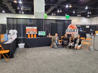 Filament team members kneeling with two goats in a trade show booth.